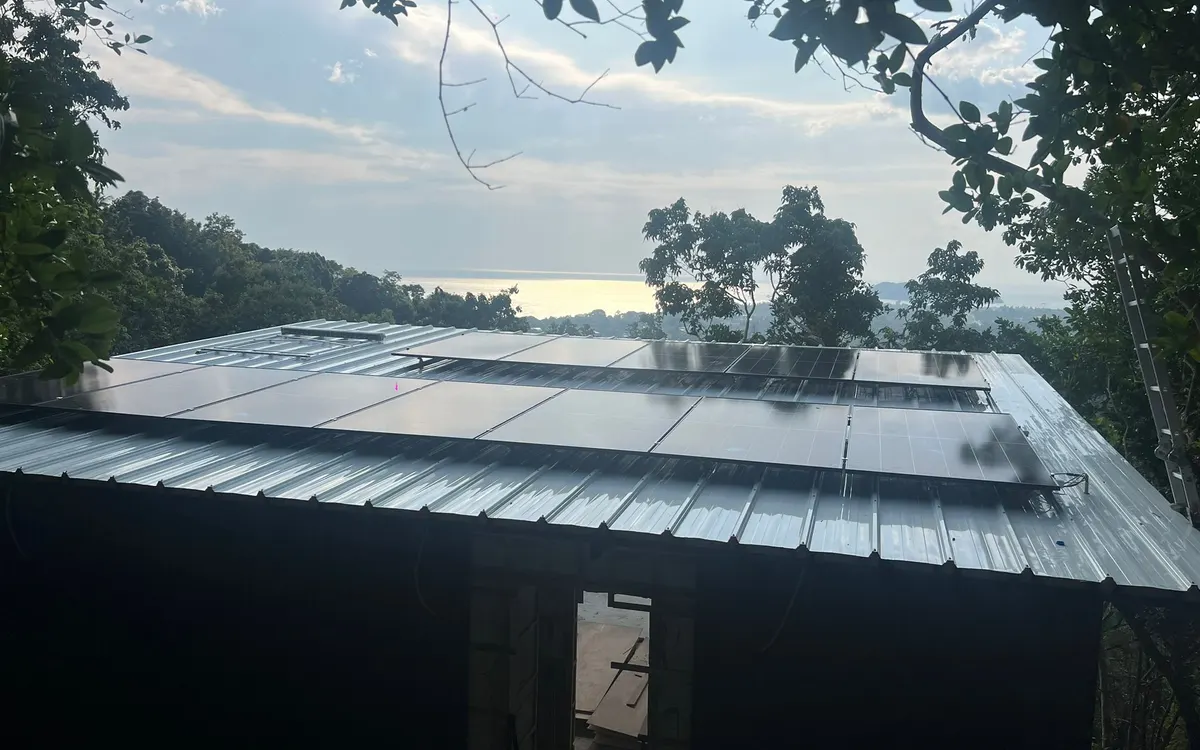 The roof of the big bungalow, covered in solar panels, with the sea behind it